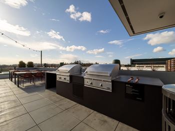 two barbecue grills on a rooftop patio with tables and chairs